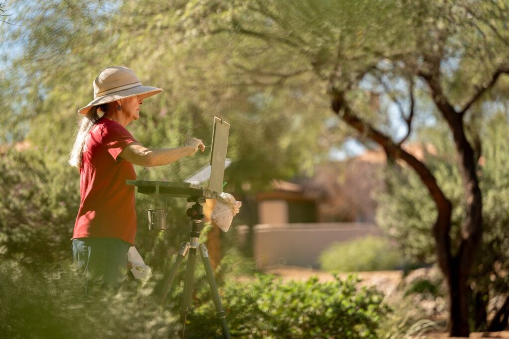 woman paints on an easel in an outdoor garden