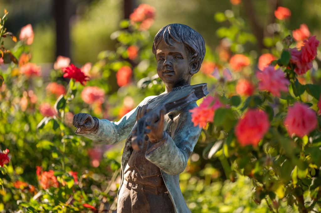 A statue of a boy with a violin, found  in the outdoors among flowers in la Posada Green Valley