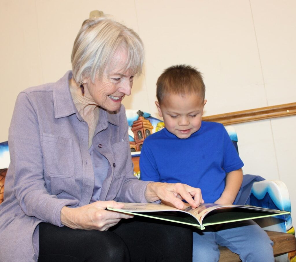 A senior woman reading a book to a younger child with a blue shirt